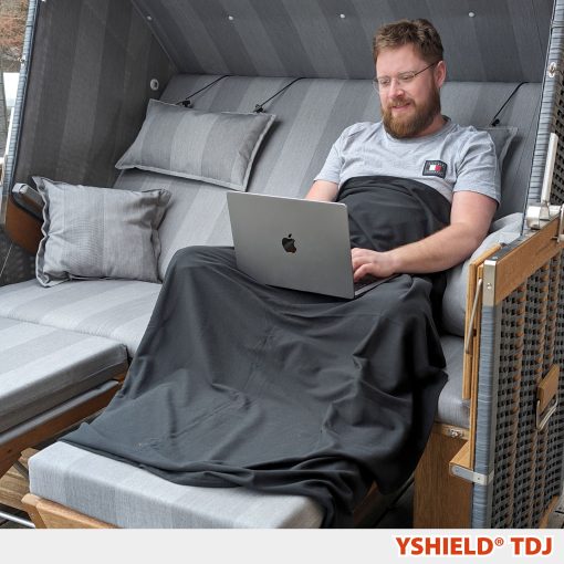 Mand i sofa med et blødt strålingsafskærmende Black-Jersey tæppe fra Yshield (100 x 140 cm) over benene